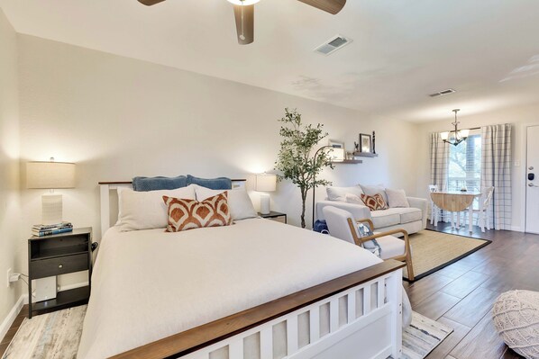 A bedroom with a large bed, bedside tables, a nightstand, a hanging chair, a small table with chairs, and a window with curtains.