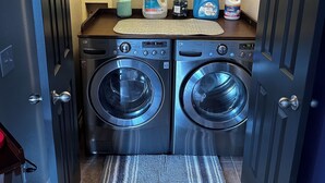 A compact laundry room with two front-loading washing machines, a countertop with cleaning supplies, and a patterned doormat. - Cozy Guest Studio with private entrance close to the Heights & TMC (Houston)