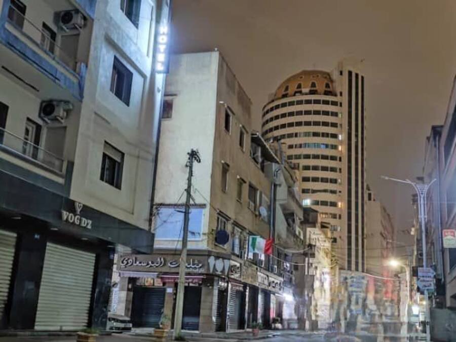 Vista nocturna de una calle con comercios cerrados y un edificio alto al fondo.
