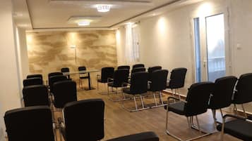 Un salón de conferencias con sillas negras dispuestas alrededor de una mesa de cristal, suelo de madera y pared de mármol.
