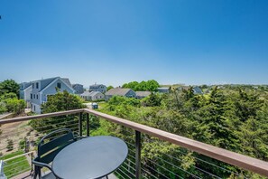 A balcony with a table and chairs, overlooking a residential area with houses and greenery. - Slow M'Ocean – A Fresh Take on Cape Calm (Chatham)