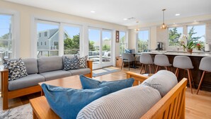 A modern living room with a sofa, a coffee table, and a dining area with chairs and a kitchen counter. - Slow M'Ocean – A Fresh Take on Cape Calm (Chatham)