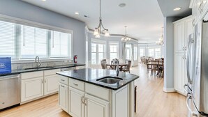 A spacious kitchen with a large island, white cabinetry, and a dining area with a table and chairs. - Over the Moon | Oceanfront | Private Pool and Hot Tub (Virginia Beach)