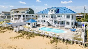 A beachfront property with multiple buildings, a swimming pool, and a beach access deck. - Over the Moon | Oceanfront | Private Pool and Hot Tub (Virginia Beach)