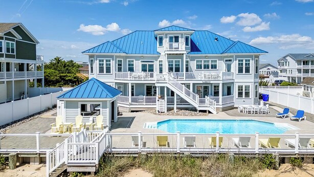 A large, multi-story house with a blue roof, a swimming pool, and a deck with lounge chairs. - Over the Moon | Oceanfront | Private Pool and Hot Tub (Virginia Beach)