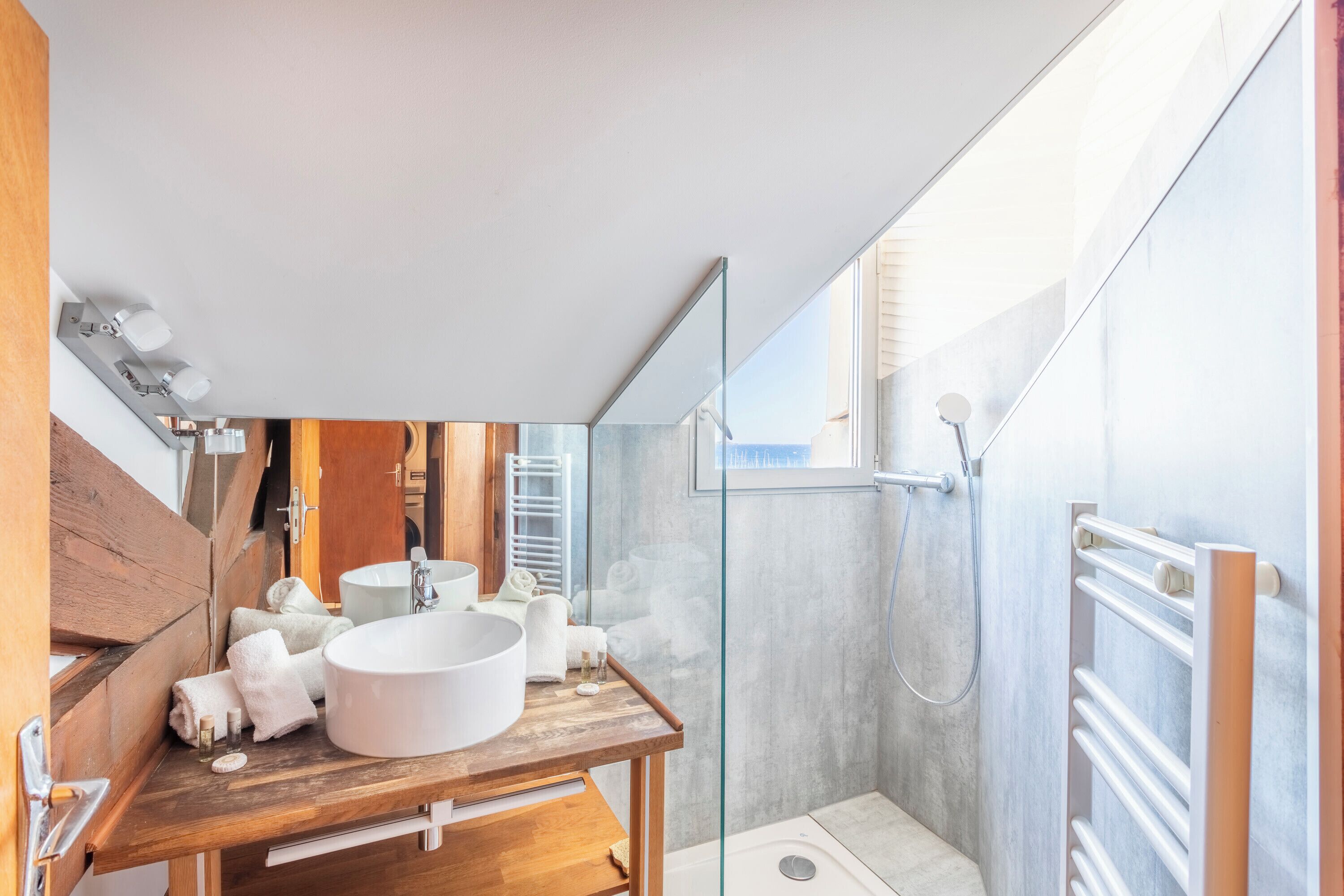 Ein modernes Badezimmer mit einem Holzausleger, einem großen weißen Waschbecken und einer Duschkabine.