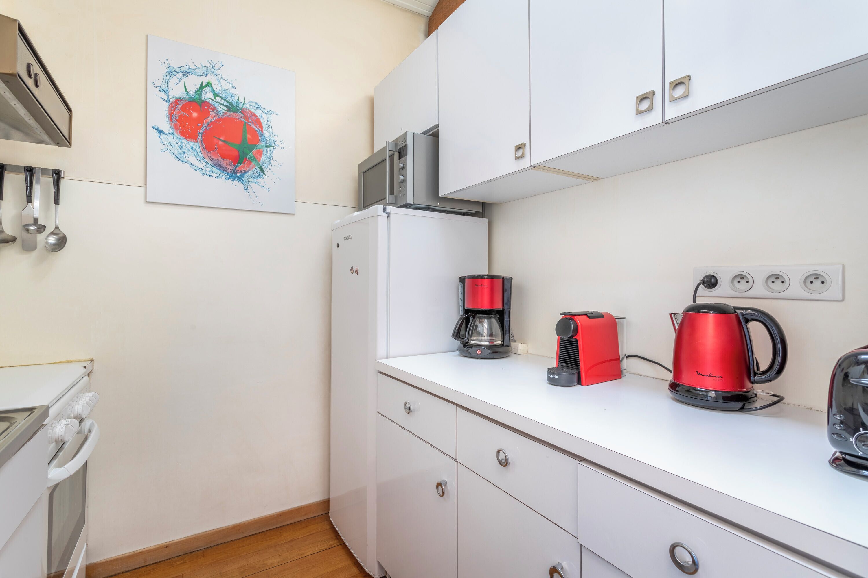 Una cocina con armarios blancos, microondas, refrigerador, cafetera y tostadora.