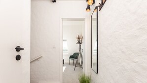A hallway with a white door, a green chair, a floor lamp, and a potted plant. - Inselkind - Appartement Inselkind (Sylt-Ost)