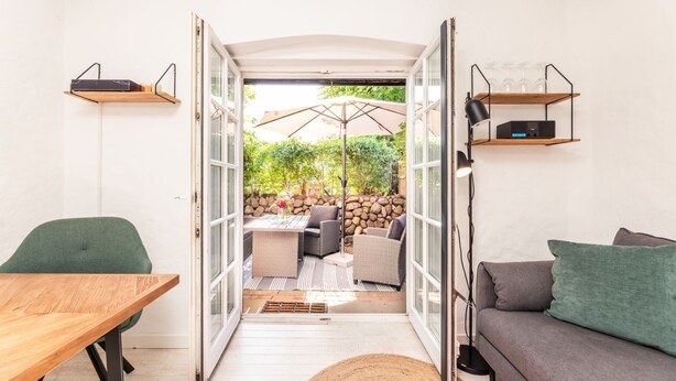 A cozy indoor space with a wooden table, a green chair, a gray sofa, and a wicker dining set. - Inselkind - Appartement Inselkind (Sylt-Ost)