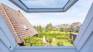 A view from a skylight of a residential area with houses, a well-maintained garden, and a clear sky. - Inselkind - Appartement Inselkind (Sylt-Ost)