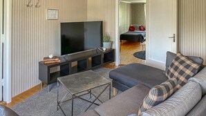 Een woonkamer met een grote flatscreen televisie, een donkere bank, een kleine salontafel en een kamerkleed met een patroon.