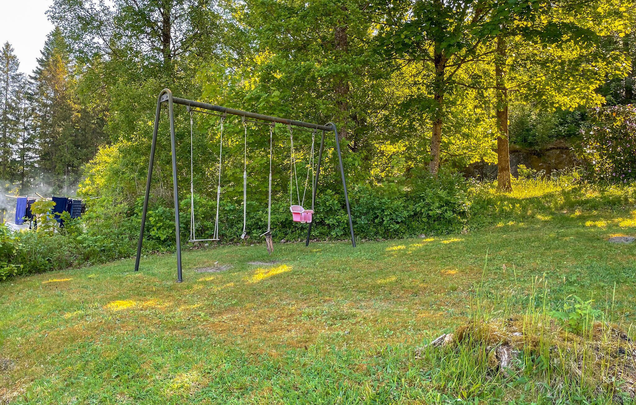 A swing set in a grassy area with trees and bushes in the background.