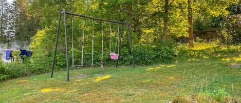 A swing set in a grassy area with trees and bushes in the background.