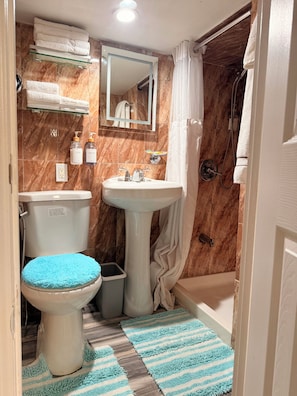 A bathroom with a toilet, sink, shower, marble walls, and a mirror.