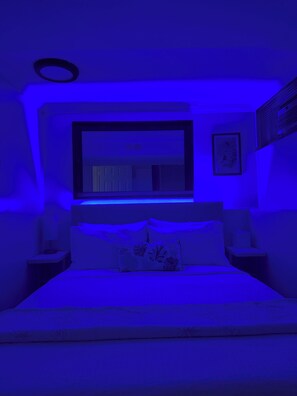 A bedroom with a bed, a nightstand, a wall-mounted TV, and a framed picture.