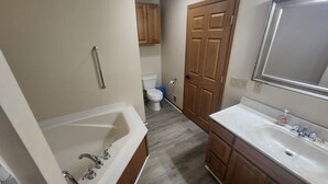 Un baño con bañera, lavamanos, armarios de madera y un inodoro.