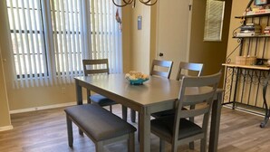 A dining area with a rectangular table, six chairs, a bench, and a window with blinds. - Water's Edge 14-3A - Two Bedroom Apartment, Sleeps 6 (Lake Ozark)