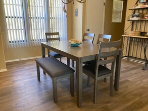A dining area with a rectangular table, six chairs, a bench, and a window with blinds. - Water's Edge 14-3A - Two Bedroom Apartment, Sleeps 6 (Lake Ozark)
