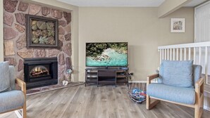 Een woonkamer met een stenen open haard, een flatscreen televisie en een houten stoel.