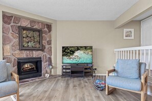 Un salon avec une cheminée en pierre, un téléviseur à écran plat et un fauteuil en bois.