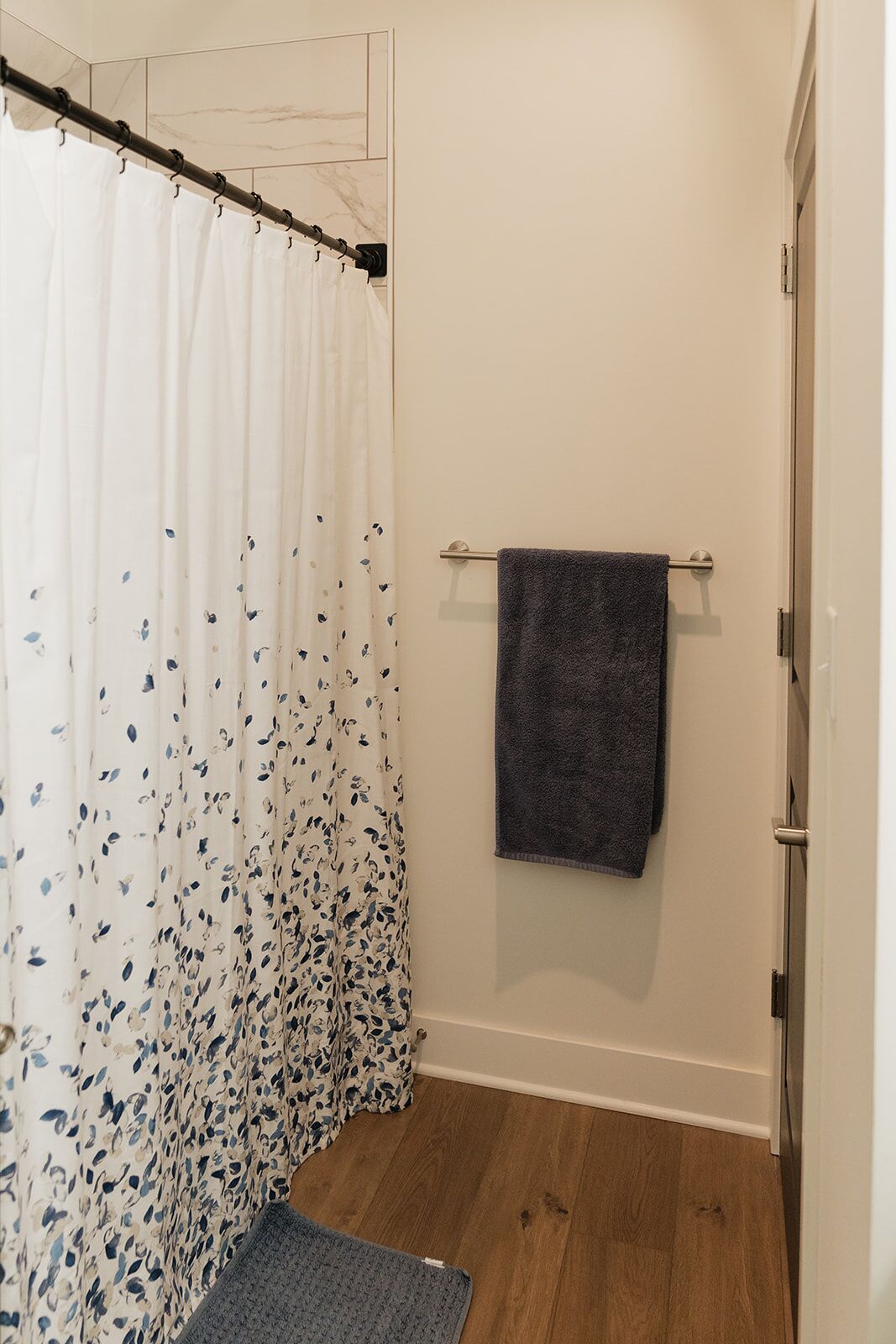 A bathroom with a shower curtain, a towel rack with a towel, and a wooden floor.