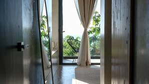 Interior moderno com piso de concreto, vista através de porta de vidro para área externa com cadeira e mesa, e porta de madeira à direita.