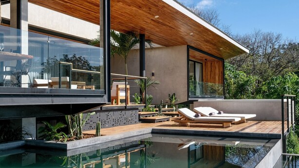 Uma casa moderna com piscina, deck de madeira e cadeiras de descanso.