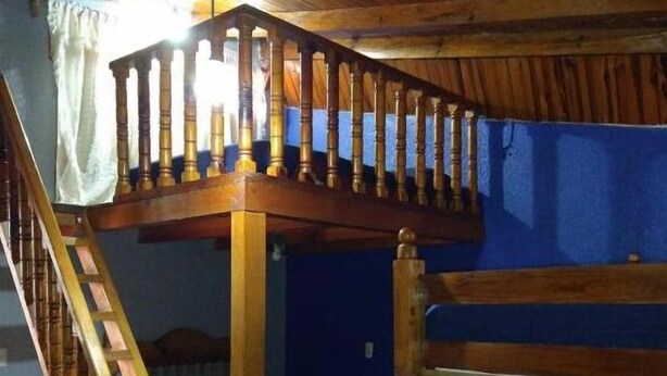 Un chalet rustique avec un escalier en bois menant à un balcon, des lits superposés et une table avec une machine à café et des tasses.