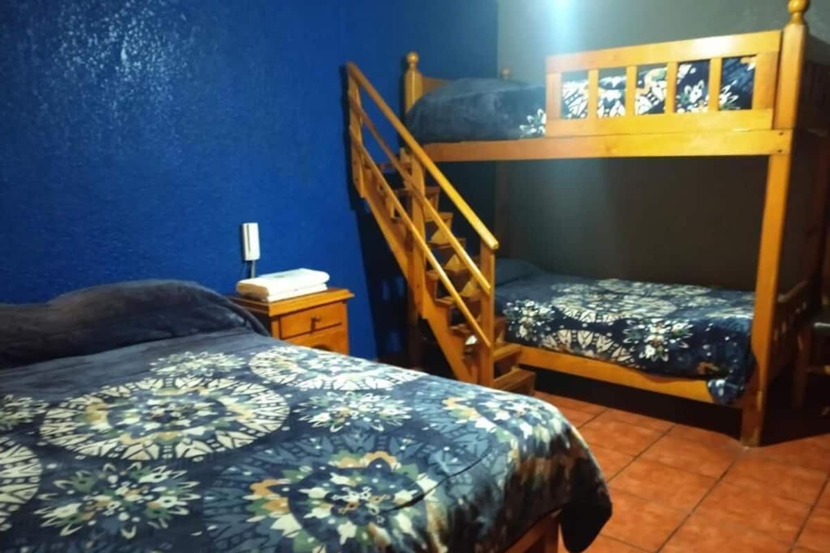 Een slaapkamer met twee bedden, een stapelbed van hout, een nachtkastje en een wandlamp.