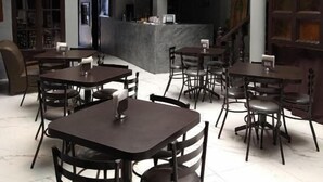 Un vaste espace dédié à la salle à manger, avec de nombreuses tables et chaises, un bar central et un escalier menant à un niveau supérieur.