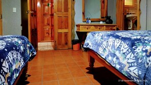 A room with two beds, a wooden door, a mirror, and a small table with items on it.