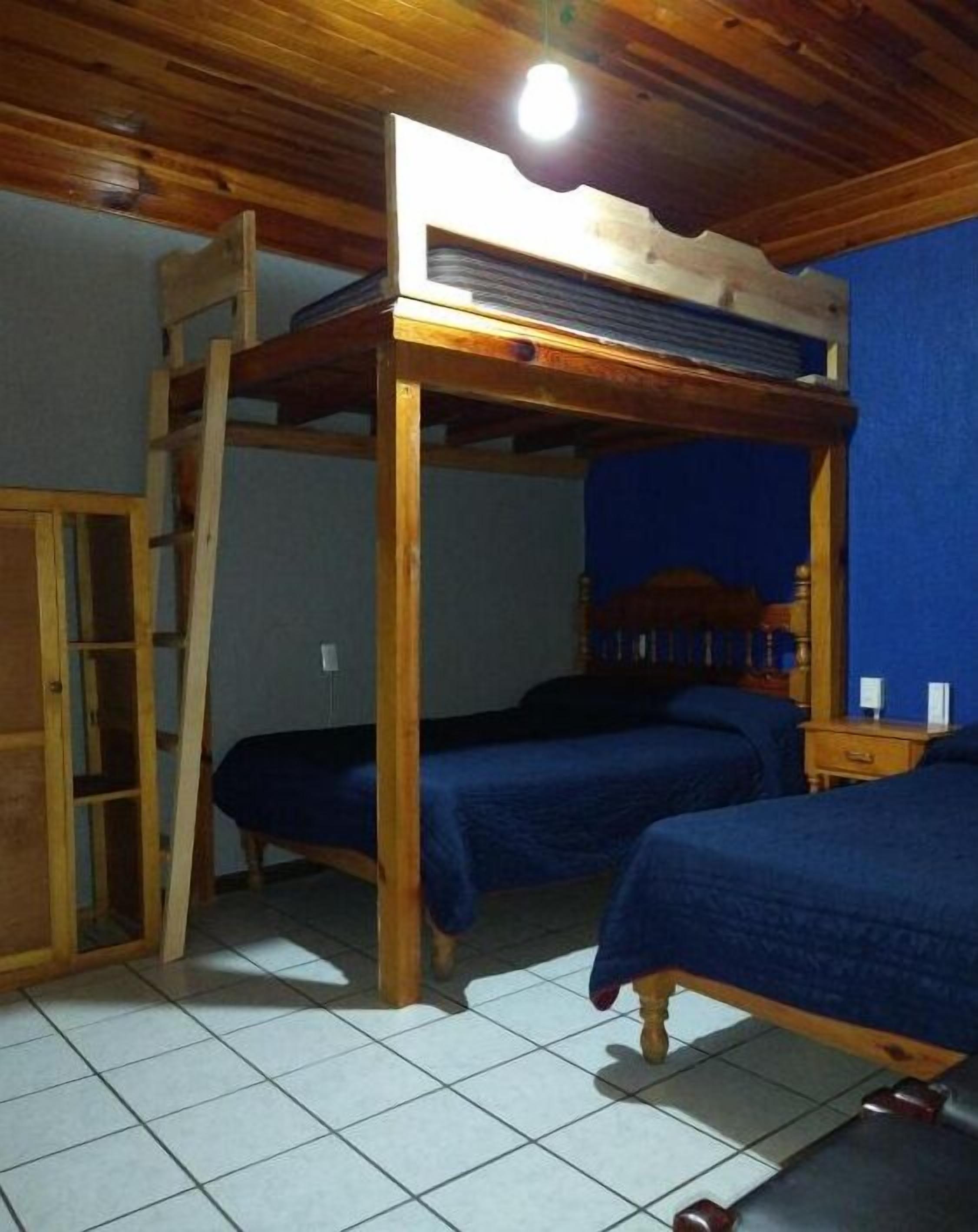 Una habitación con una cama individual superpuesta, una escalera, una mesita pequeña y una pared azul.