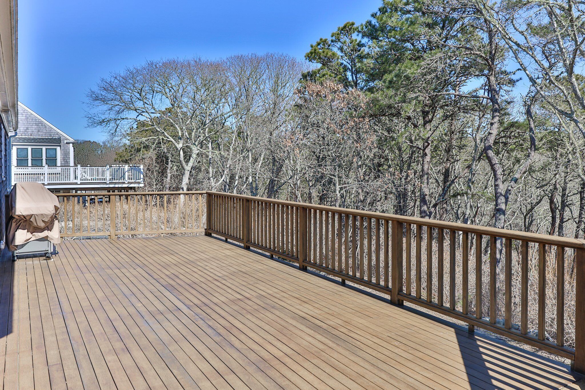 A wooden deck with a railing, a covered seating area, and a view of trees and a house in the background.