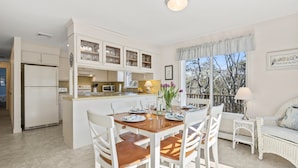A kitchen with white cabinets, a dining table set with plates and glasses, and a view of trees through the window.
