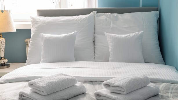 A neatly made bed with white linens and towels, a grey headboard, and a lamp on the nightstand. - National Stadium Comfy Apartment (Warszawa)