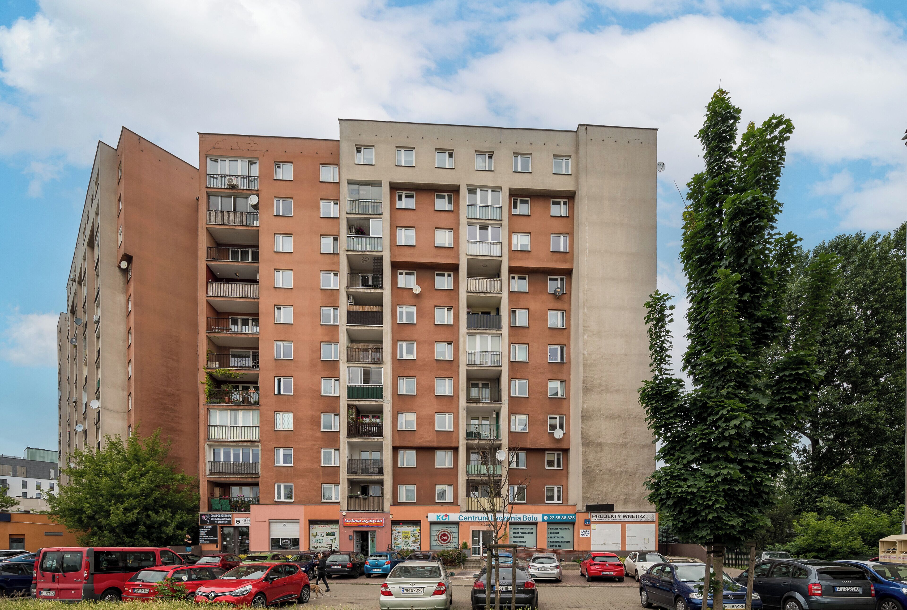 A multi-story residential building with balconies and a parking lot in front.