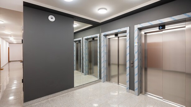 Een modern liftgedeelte met een gepolijste vloer, metalen liftdeuren en verlichting in het plafond.