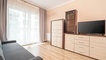 Ein modernes Wohnzimmer mit einer Couch, einem Flachbildfernseher, einem Schrank und einem großen Fenster mit transparenten Vorhängen.