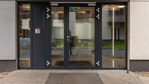 Een moderne gevel met glazen deur, een metalen beveiligingspoort en een bord dat een wachtruimte aangeeft.