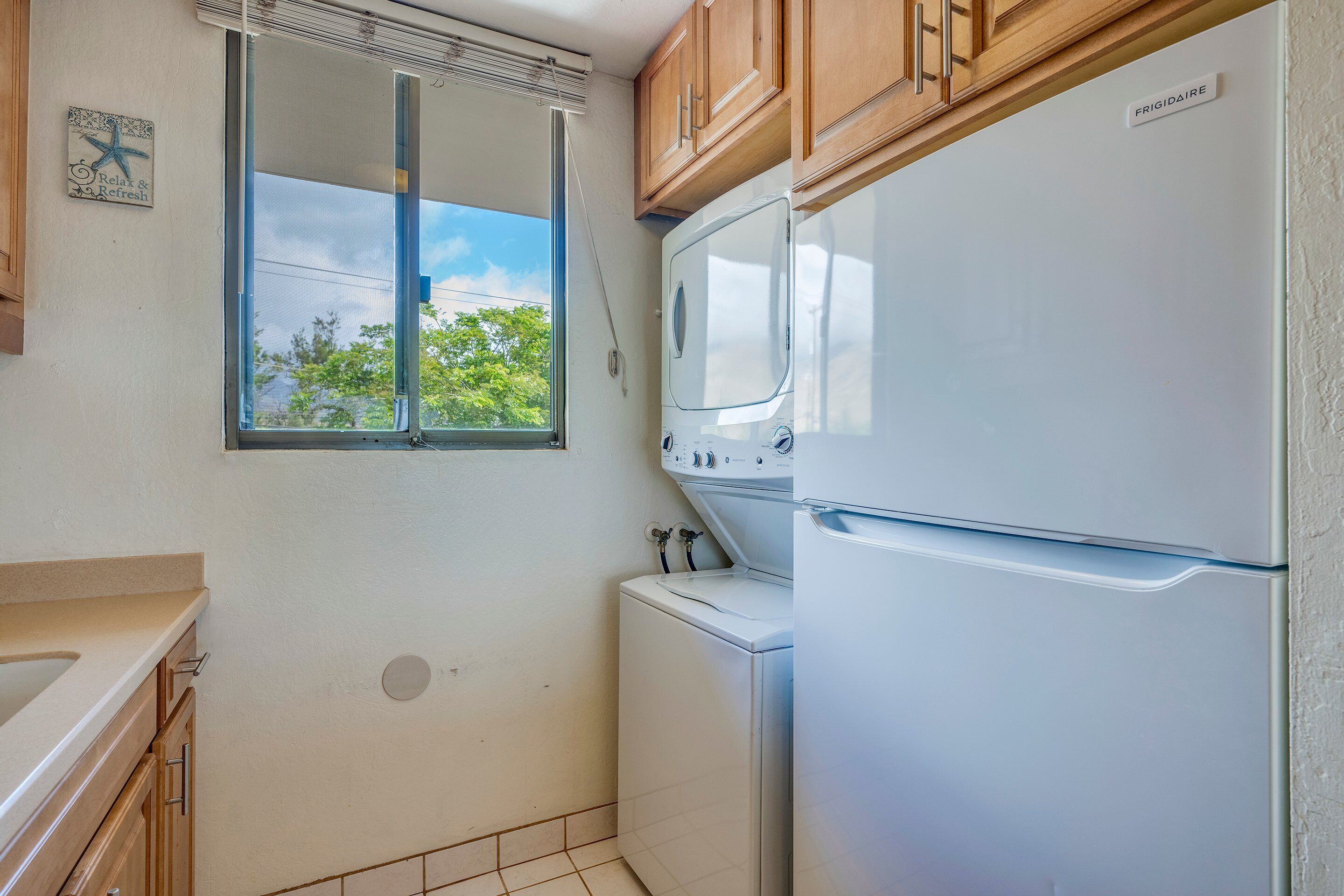 A compact kitchen with a window, a washing machine, and a refrigerator.