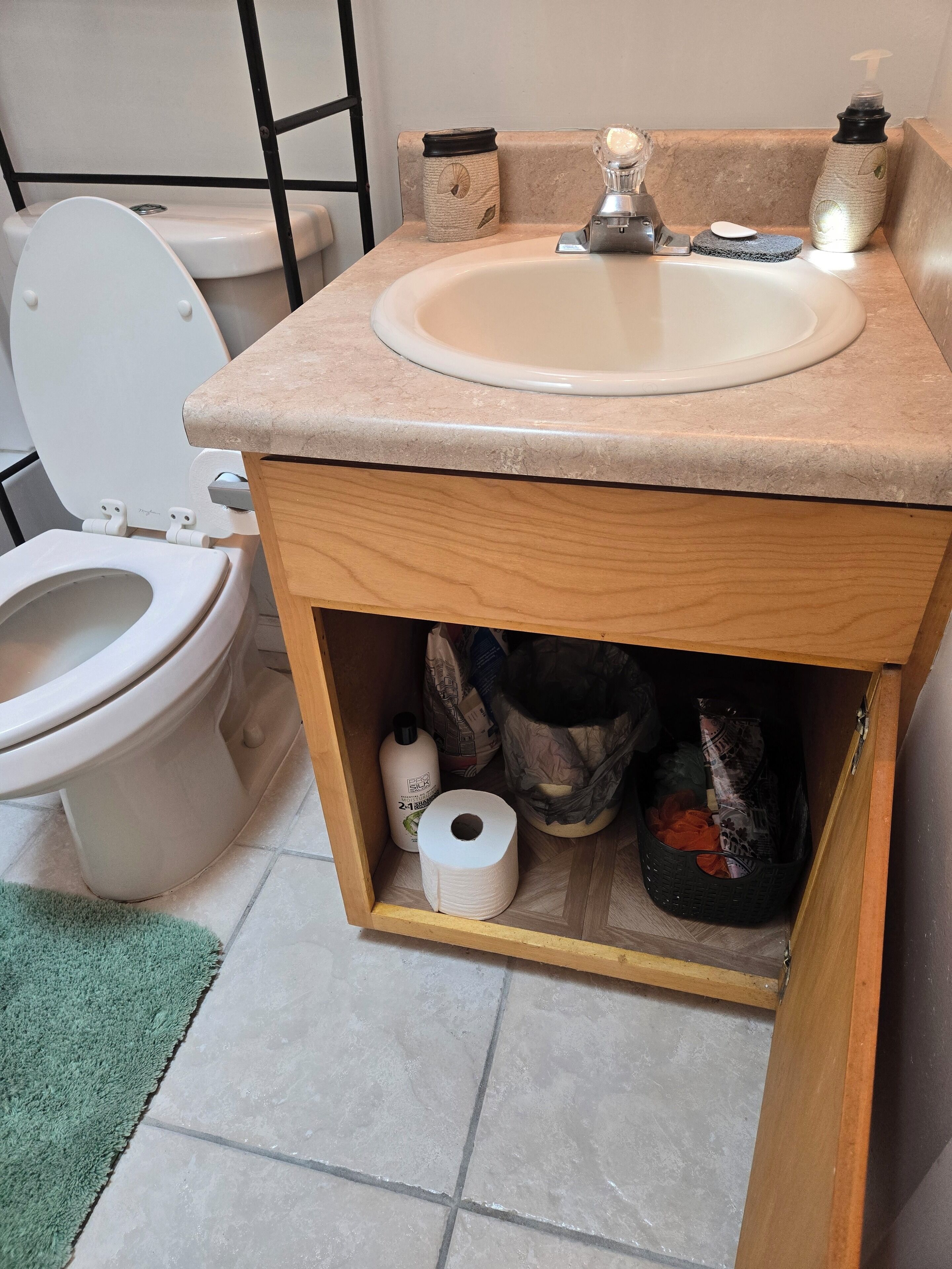 A bathroom with a toilet, sink, and storage cabinet.