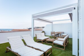 A rooftop terrace with white cushioned lounge chairs, a wooden table, and chairs. - Casa Checha Charming Penthouse With Breathtaking Views (Candelaria)