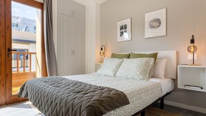 Un dormitorio con una cama, una mesita de noche, una lámpara y una puerta a un balcón.