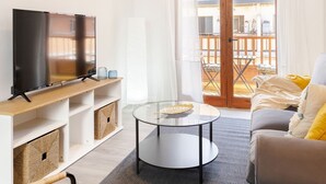 Una sala de estar moderna con televisor de pantalla plana, una mesa redonda de centro, sillas de mimbre y un sofá con almohadas amarillas.