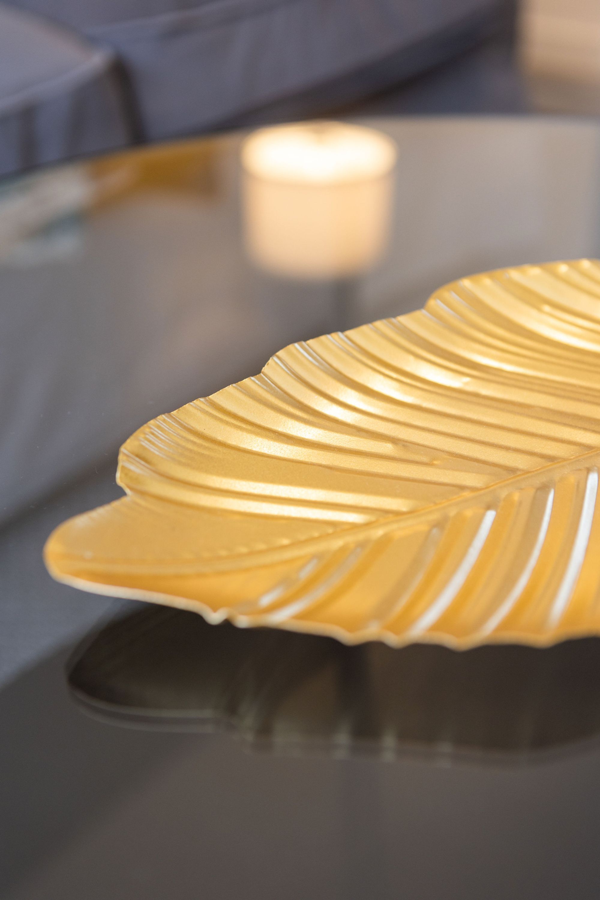 A close-up of a golden, ribbed object on a reflective surface, possibly a decorative item, with a blurred background featuring a soft light source.