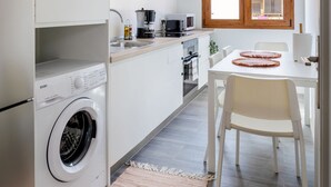 Una cocina funcional con lavadora, una zona de comedor con mesa y sillas, y un ventanal con marcos de madera.