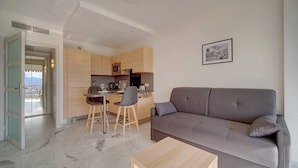 Una sala de estar moderna con un sofá gris, una mesa de centro de madera y un comedor con una cocina al fondo.