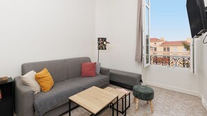 Een moderne woonkamer met een grijze bank, een klein houten tafeltje en een balkon met uitzicht op gebouwen.