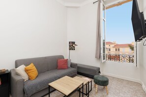 A modern living room with a grey sofa, a small wooden table, and a balcony with a view of buildings.