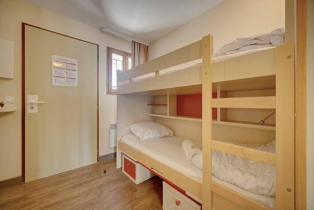 A dormitory room with bunk beds, a door with a notice, and a window with curtains.